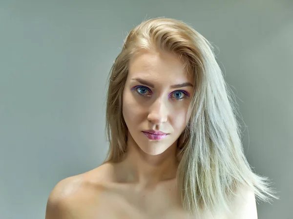 Concepto de retrato de cerca de una hermosa chica rubia sobre un fondo gris. El cabello se desarrolla en diferentes direcciones . — Foto de Stock