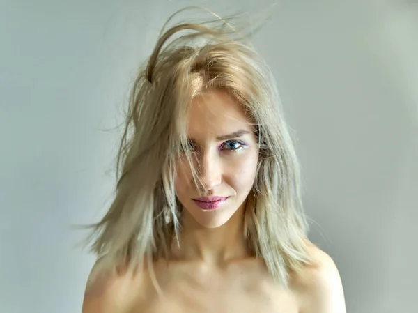 Closeup portrait concept of a beautiful blonde girl on a gray background. Hair develops in different directions. — Stock Photo, Image