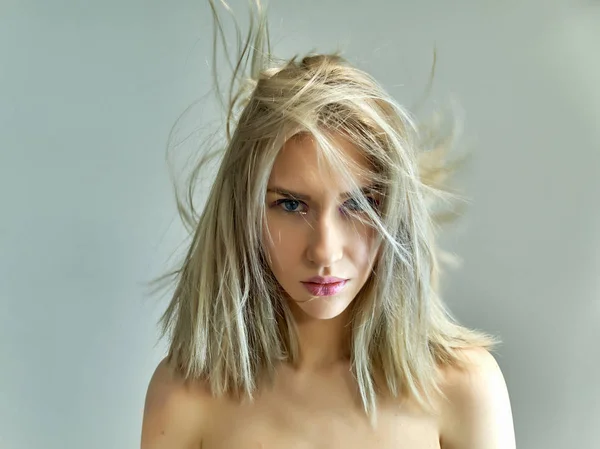 Концепция крупным планом красивой блондинки на сером фоне. Волосы развиваются в разных направлениях . — стоковое фото