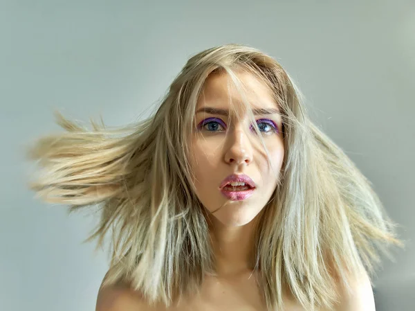 Närbild porträtt begreppet en vacker blond flicka på en grå bakgrund. Hår utvecklas i olika riktningar. — Stockfoto