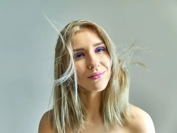 Concepto de retrato de cerca de una hermosa chica rubia sobre un fondo gris. El cabello se desarrolla en diferentes direcciones . — Foto de Stock