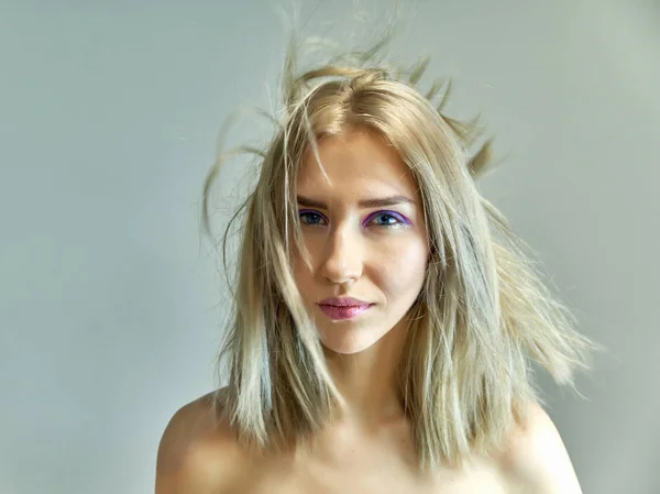 Nahaufnahme Portraitkonzept eines schönen blonden Mädchens auf grauem Hintergrund. Haare entwickeln sich in verschiedene Richtungen. — Stockfoto