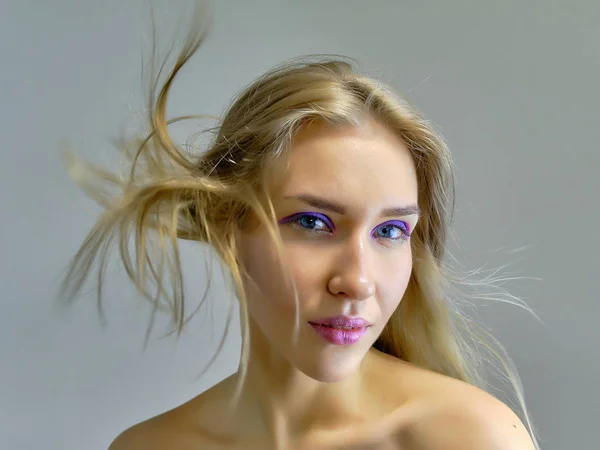 Closeup portret concept van een mooi blond meisje op een grijze achtergrond. Haar ontwikkelt zich in verschillende richtingen. — Stockfoto