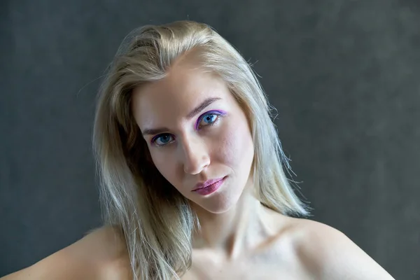 Conceito de retrato close-up de uma linda garota loira em um fundo cinza. O cabelo se desenvolve em diferentes direções . — Fotografia de Stock