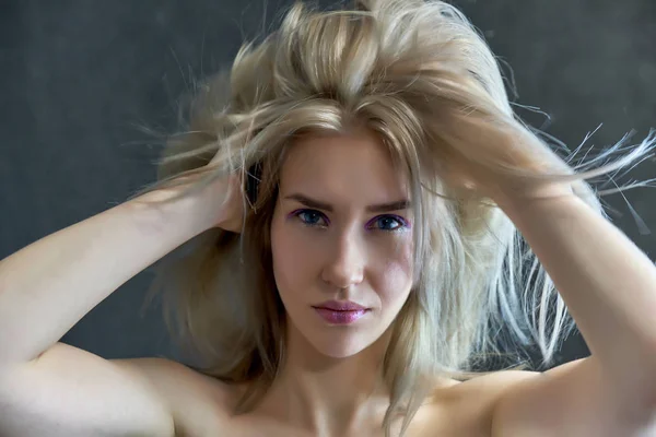 Närbild porträtt begreppet en vacker blond flicka på en grå bakgrund. Hår utvecklas i olika riktningar. — Stockfoto