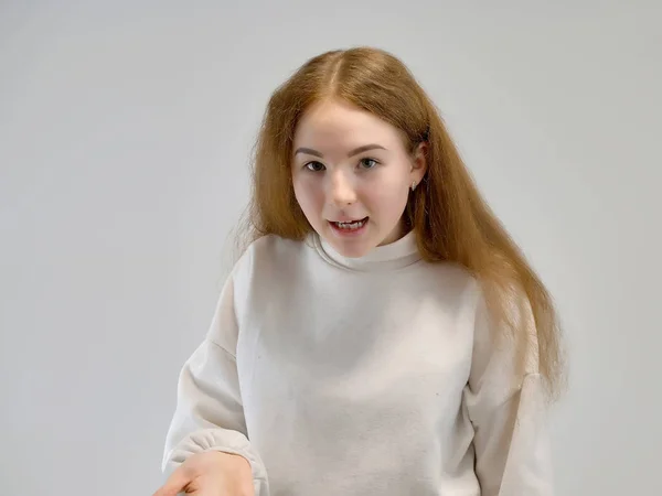 Concepto retrato de una linda chica adolescente con el pelo rojo contra el fondo gris sonriendo y hablando . —  Fotos de Stock