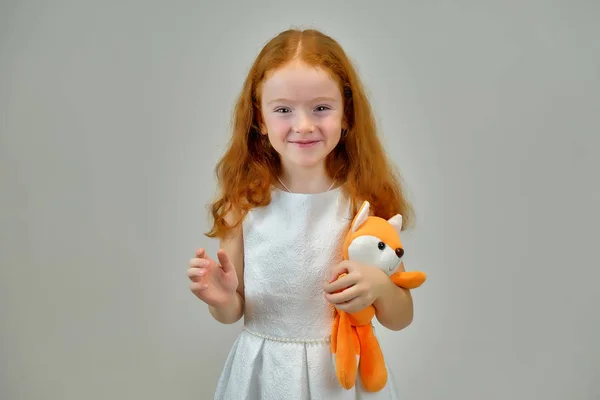 Retrato conceptual de una linda niña bonita con el pelo rojo sobre un fondo gris sonriendo y hablando —  Fotos de Stock