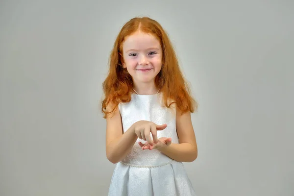 Retrato conceptual de una linda niña bonita con el pelo rojo sobre un fondo gris sonriendo y hablando —  Fotos de Stock