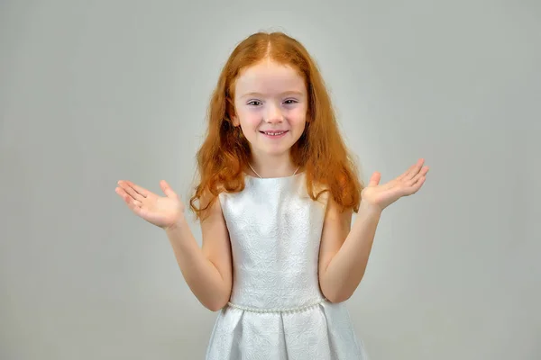 Begreppet porträtt av en söt vackra barn flicka med rött hår på en grå bakgrund ler och talar — Stockfoto
