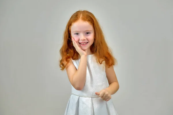 Retrato conceptual de una linda niña bonita con el pelo rojo sobre un fondo gris sonriendo y hablando —  Fotos de Stock