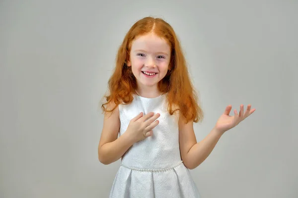 Concept portrait of a cute pretty child girl with red hair on a gray background smiling and talking — Stock Photo, Image