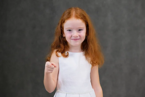 Retrato conceptual de una linda niña bonita con el pelo rojo sobre un fondo gris sonriendo y hablando —  Fotos de Stock