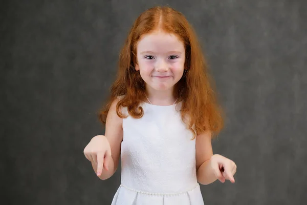 Концептуальный портрет милой красивой девочки с рыжими волосами на сером фоне, улыбающейся и говорящей — стоковое фото
