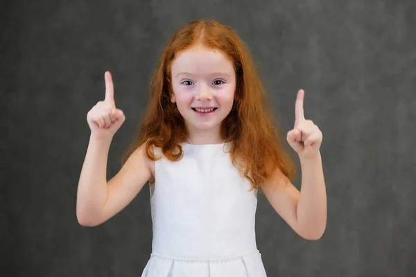 Egy aranyos szép gyermek lány, vörös haj, egy szürke háttér, mosolyogva, és beszélt koncepció portréja — Stock Fotó