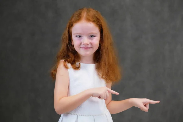 Concept portrait of a cute pretty child girl with red hair on a gray background smiling and talking — Stock Photo, Image