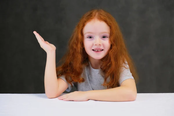 Concept portrait of a cute pretty child girl with red hair on a gray background smiling and talking. — Stock Photo, Image