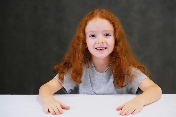 Concept retrato de uma menina bonita bonito com cabelo vermelho em um fundo cinza sorrindo e falando . — Fotografia de Stock