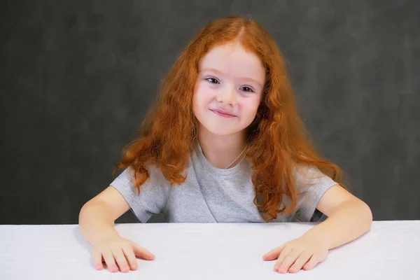 Concept portrait of a cute pretty child girl with red hair on a gray background smiling and talking. — Stock Photo, Image