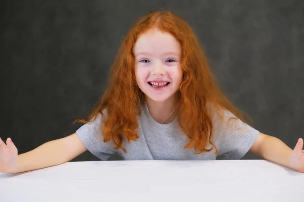 Concept portrait of a cute pretty child girl with red hair on a gray background smiling and talking. — Stock Photo, Image