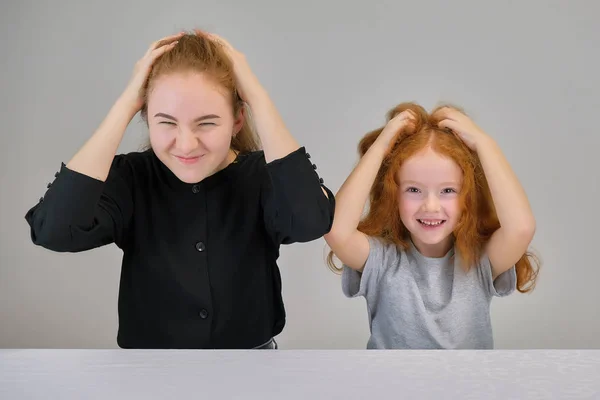 Concept portrait of two cute pretty girls sisters with red hair on a gray background smiling and talking.