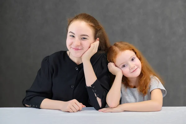 Концептуальний портрет двох симпатичних дівчат-сестер з рудим волоссям на сірому фоні, посміхаючись і розмовляючи . — стокове фото