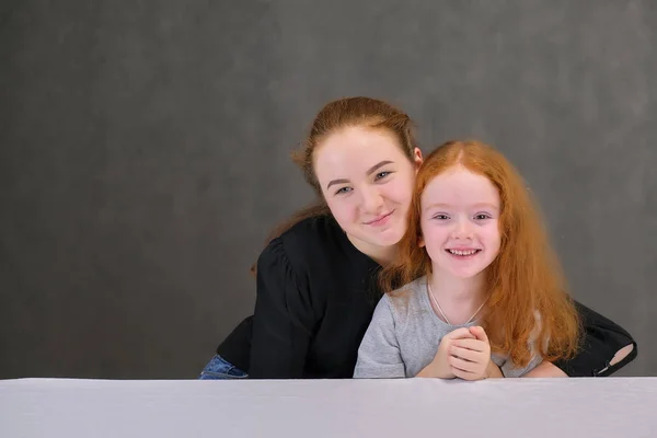 Concept portrait of two cute pretty girls sisters with red hair on a gray background smiling and talking.