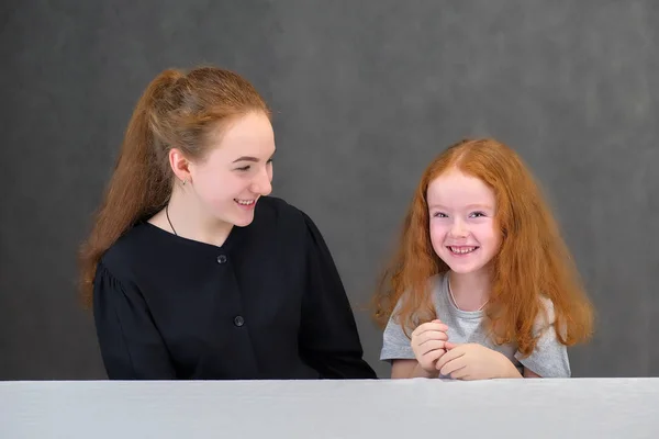 Concepto retrato de dos lindas hermanas guapas con el pelo rojo sobre un fondo gris sonriendo y hablando . —  Fotos de Stock