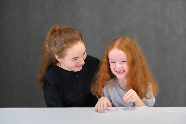 Concepto retrato de dos lindas hermanas guapas con el pelo rojo sobre un fondo gris sonriendo y hablando . —  Fotos de Stock