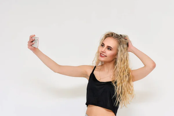 Concetto ritratto di una bella ragazza bionda su uno sfondo bianco fa selfie su uno smartphone . — Foto Stock