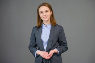 Gri arka plan üzerinde duran bir güzel genç iş kadın portresi. Doğal makyaj ve güzel bir gülümseme ile mutlu gülen genç kız.