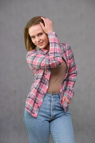 Portrait of soncept young cheerful long-haired brunette woman in casual clothes in tight blue jeans and a checkered shirt. — Stock Photo, Image