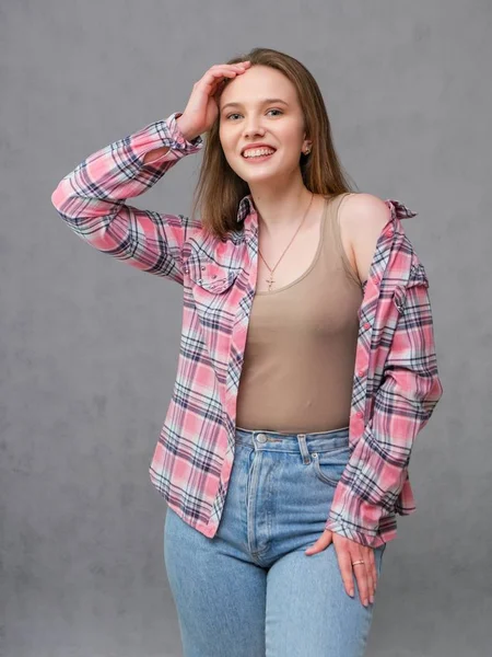 Retrato de soncept joven alegre morena de pelo largo en ropa casual en vaqueros azules ajustados y una camisa a cuadros . —  Fotos de Stock