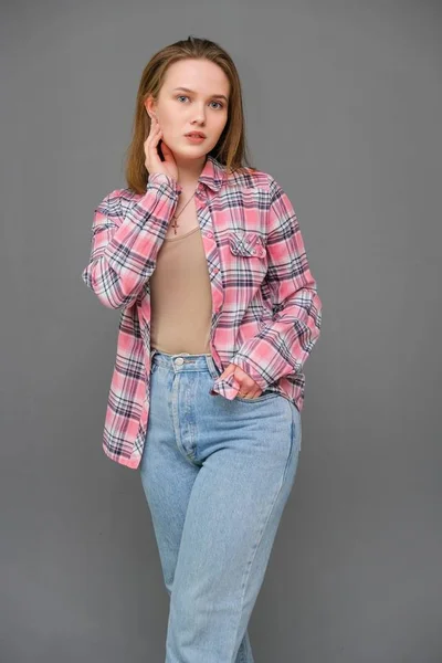 Portret van soncept jonge vrolijke langharige brunette vrouw in casual kleding in strakke spijkerbroek en een geruite shirt. — Stockfoto