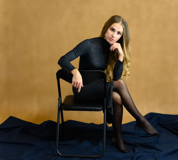 Portrait of a beautiful blonde girl sitting on a chair in the studio. Art, beauty. White chair, beige background. — Stock Photo, Image