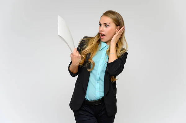 Ritratto di una graziosa segretaria finanziaria bionda con lunghi capelli ricci in un abito da lavoro in piedi in studio su uno sfondo bianco con emozioni in pose diverse con una cartella in mano . — Foto Stock