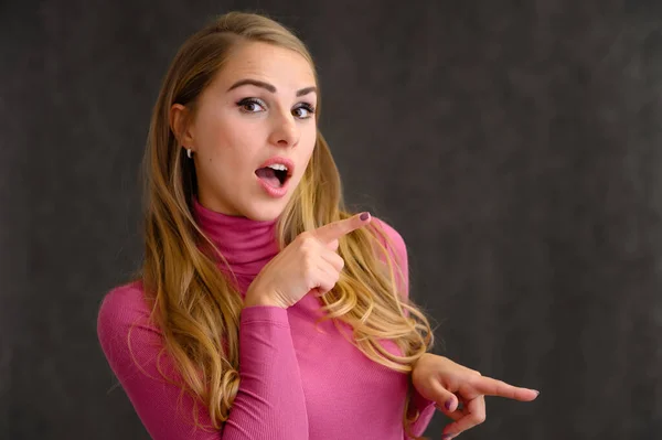 Retrato close-up de uma linda garota loira com cabelos longos encaracolados em pé no estúdio em um fundo cinza com emoções em diferentes poses em uma camisola rosa. Beleza, Modelo, Cosméticos — Fotografia de Stock