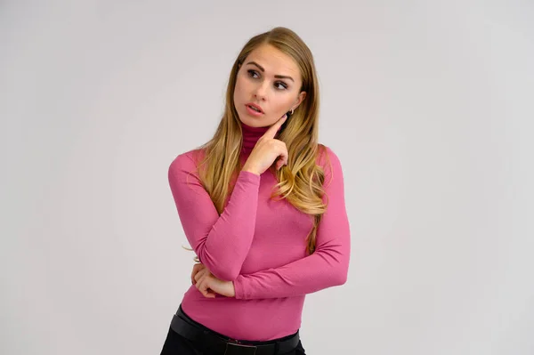 Retrato de cerca de una bonita chica rubia con el pelo rizado largo de pie en el estudio sobre un fondo blanco con emociones en diferentes poses en un suéter rosa. Belleza, Modelo, Cosméticos — Foto de Stock