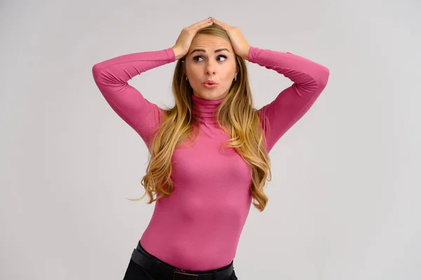 Retrato de cerca de una bonita chica rubia con el pelo rizado largo de pie en el estudio sobre un fondo blanco con emociones en diferentes poses en un suéter rosa. Belleza, Modelo, Cosméticos —  Fotos de Stock