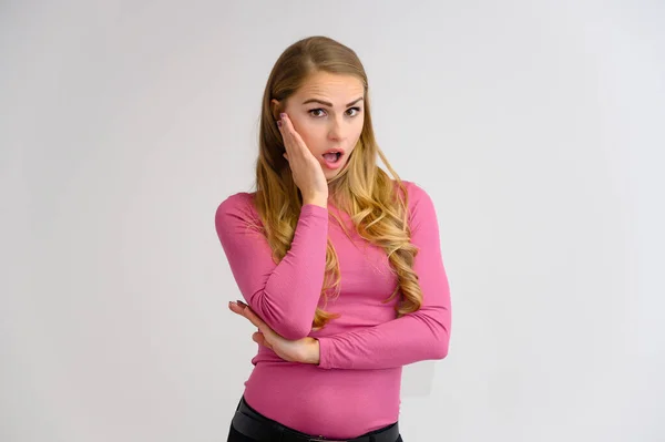 Retrato close-up de uma linda garota loira com cabelos longos encaracolados em pé no estúdio em um fundo branco com emoções em diferentes poses em uma camisola rosa. Beleza, Modelo, Cosméticos — Fotografia de Stock