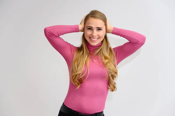 Retrato de cerca de una bonita chica rubia con el pelo rizado largo de pie en el estudio sobre un fondo blanco con emociones en diferentes poses en un suéter rosa. Belleza, Modelo, Cosméticos — Foto de Stock