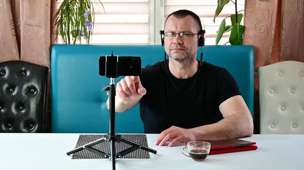 Kaukasische jongeman in een zwart T-shirt zit op een bank en zet een draadloze headset op — Stockfoto