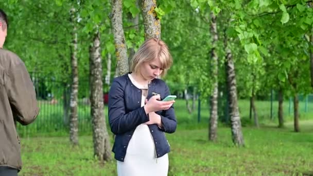 Relationship problems. A woman does not talk to a man. Young couple are walking in the park using smartphones. The concept of family communication — Stock Video