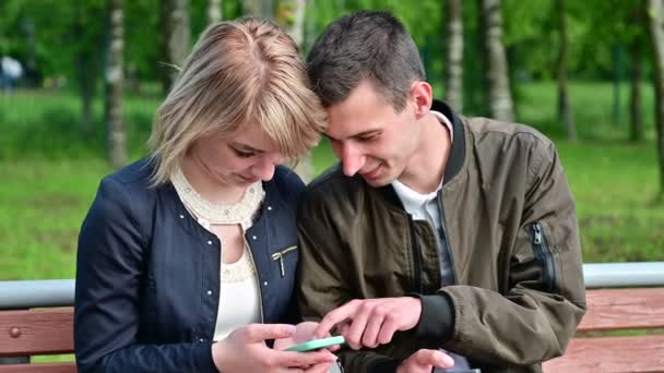 Young couple use a smartphone while sitting on a bench in the park. The concept of family communication. Relationship problems — Αρχείο Βίντεο