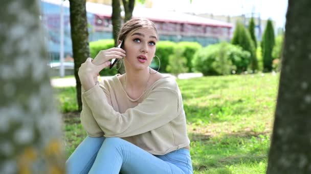 Photo of a fashionable stylish woman talking on the phone. Vogue Caucasian girl with excellent make-up sits on in a city park under the sun — kuvapankkivideo