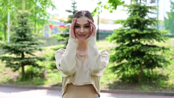 Foto modieuze stijlvolle vrouw. Een blank meisje met een uitstekende make-up met een glimlach staat in een stadspark onder de zon. — Stockvideo