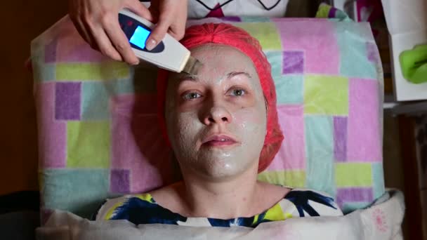 Den kosmetolog masserar ansiktet på enheten med den kvinnliga patienten. Ovanifrån. — Stockvideo