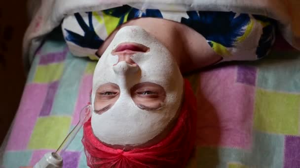 Esteticista de vídeo em um sofá faz uma massagem facial com um dispositivo de máscara . — Vídeo de Stock