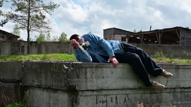 Een man met een gasmasker op de achtergrond van het verwoeste verlaten gebouw. Een man staat langzaam op en gaat zitten. — Stockvideo