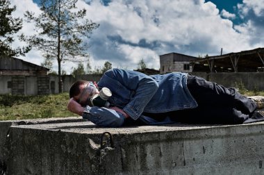 Biyolojik tehlike kavramı. Gaz maskeli bir adam harabelerin ve dramatik gökyüzü arka planının arasında yatıyor. Çevre kirliliği, ekolojik felaket, radyasyon.