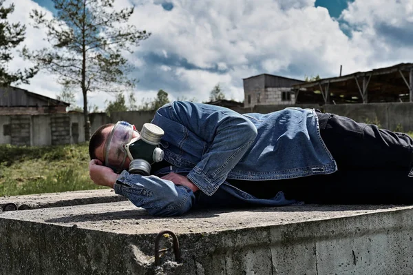 Photo of the ruins of a building. A man in a protective mask lies on the ruins in sunny weather